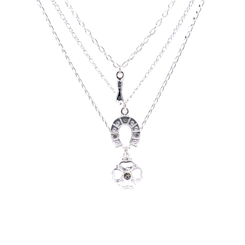 The Good Luck Charms Pendant Stacked Necklace, measuring 17 inches and silver-plated, features three delicate chains. The longest chain boasts a horseshoe charm for good fortune, embellished with small stones and a flower-shaped charm centering a stone. The other chains enhance the design with their layered elegance.